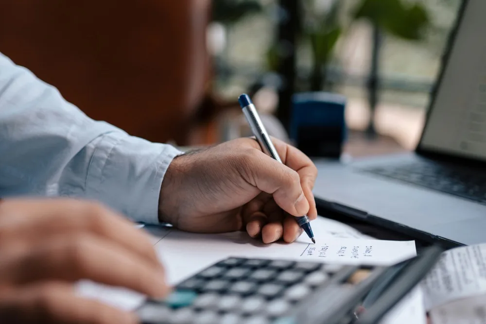 Hands writing figures beside a calculator