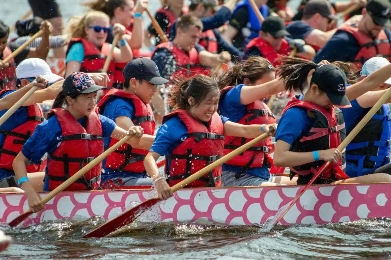 A youth dragon boat crew in life jackets paddling in unison during a festival race.