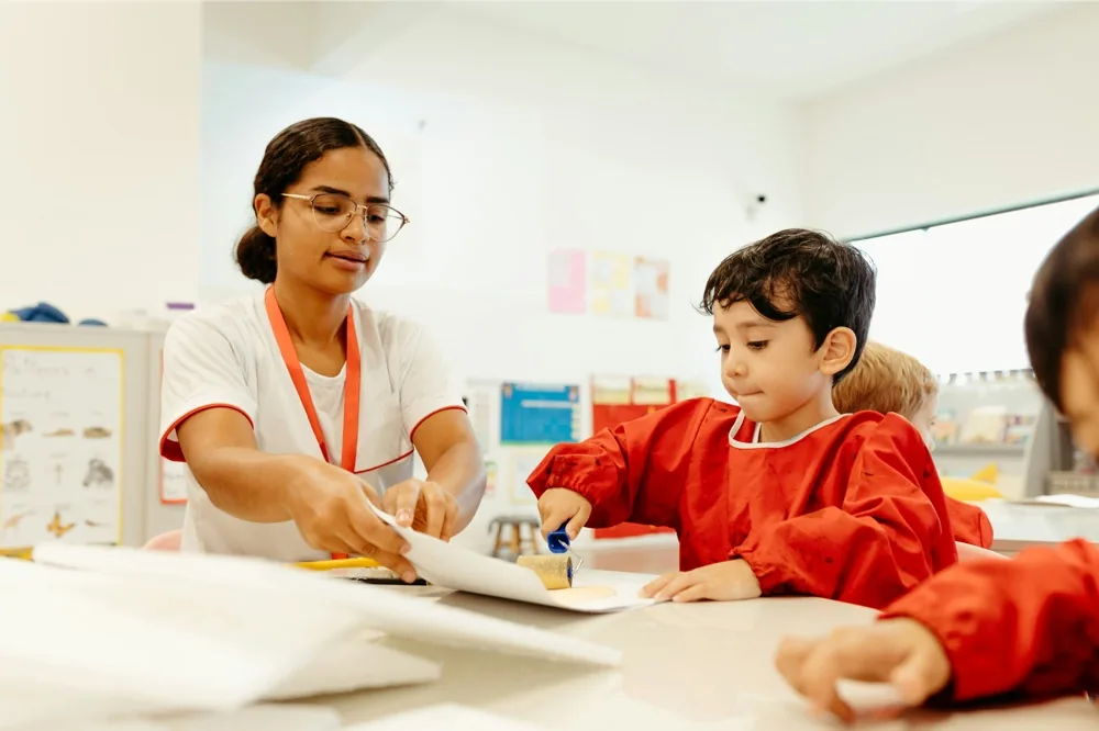 A teacher leaning in to help a student at a classroom desk