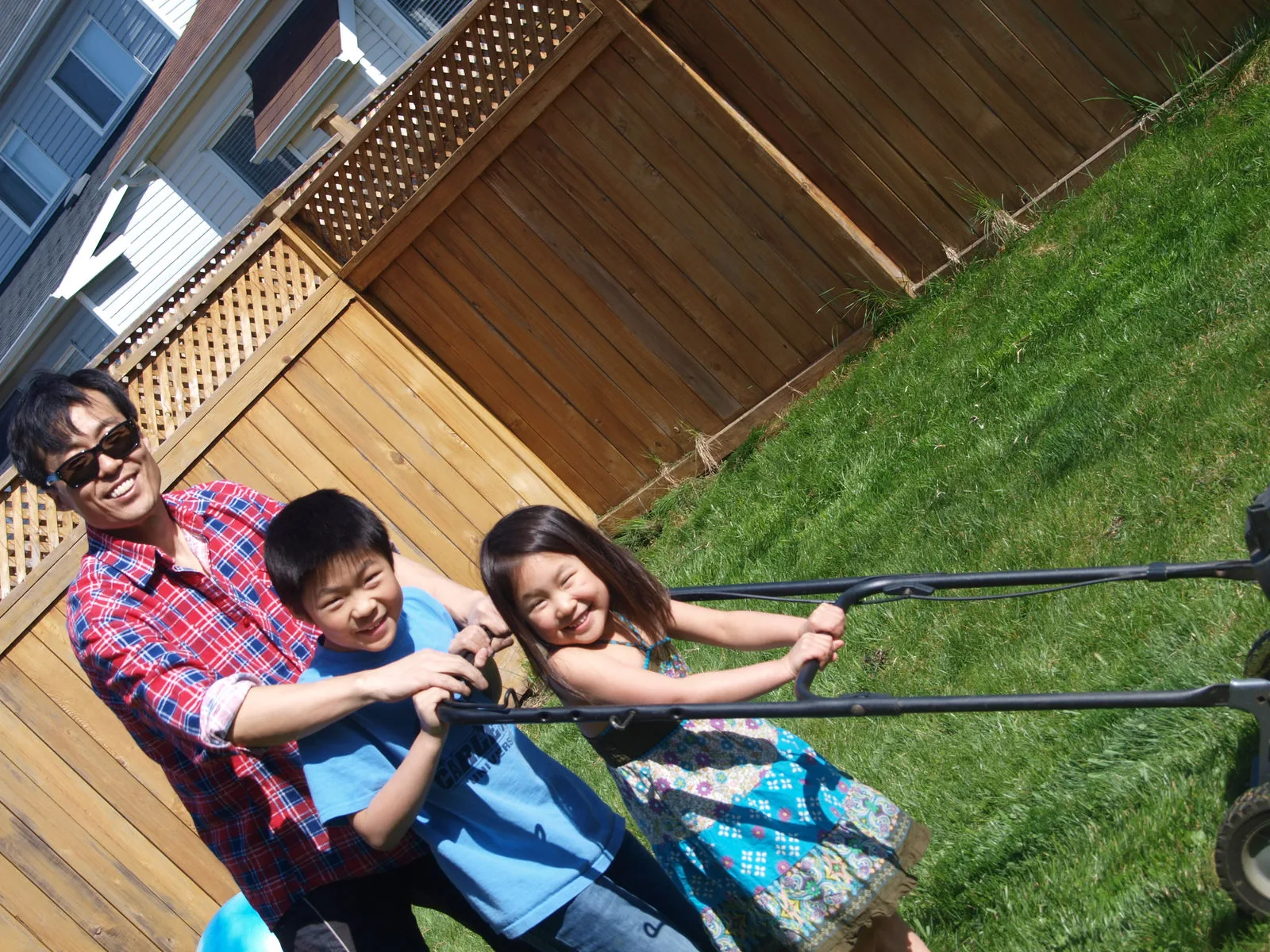 Two children riding a backyard zipline together while a parent steadies them.