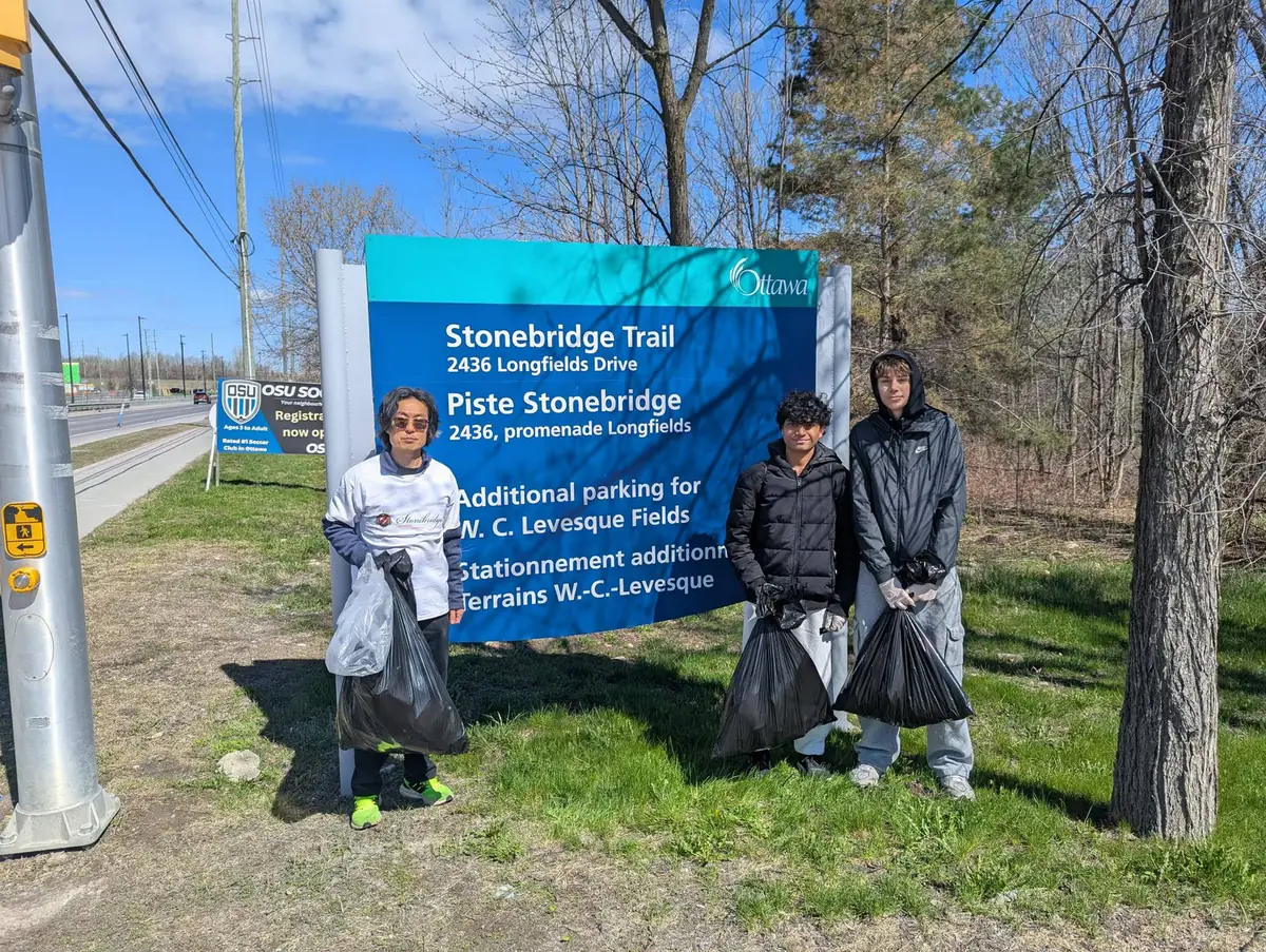 Volunteers in high-visibility gear standing beside the Stonebridge Trail sign on a spring morning.