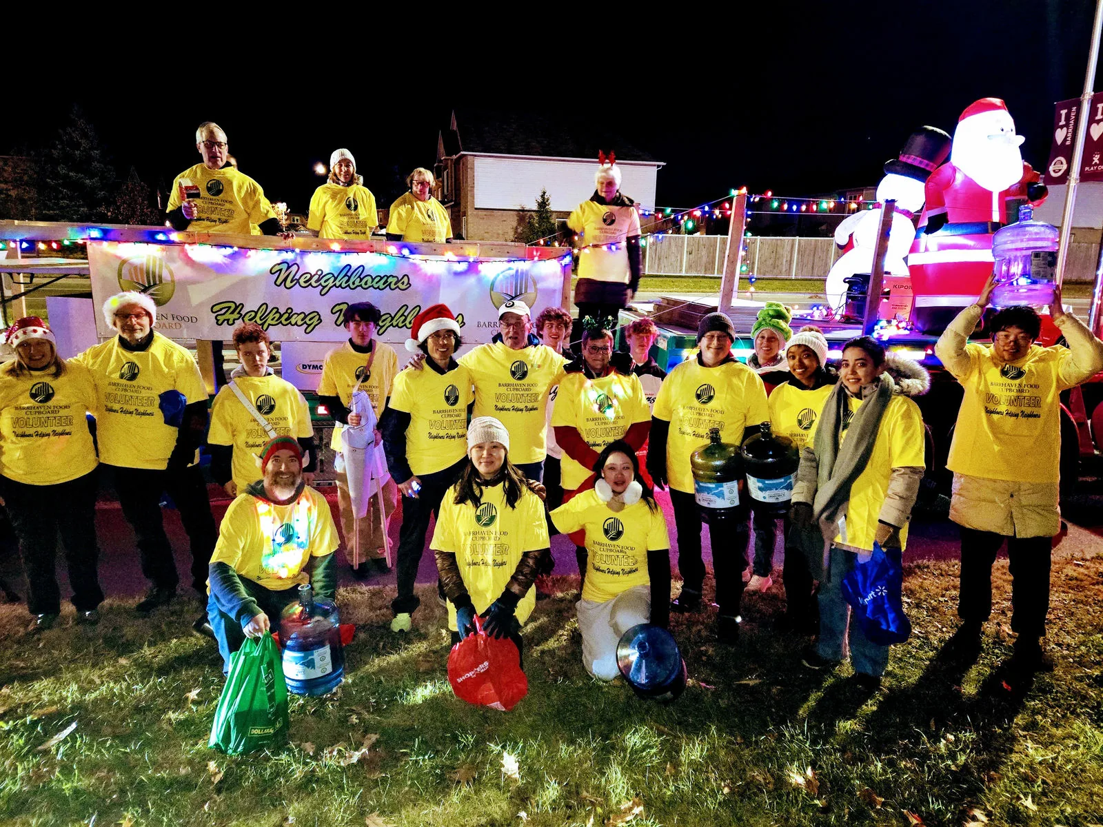 A large group of young people in matching yellow team shirts gathered outdoors at an evening community event.